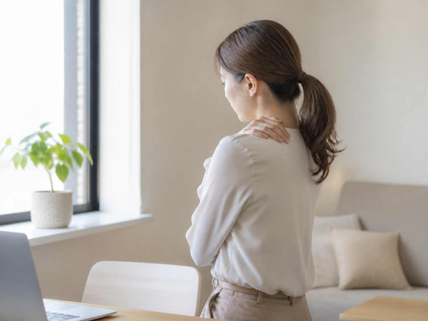 窓辺で肩に手を当てる女性